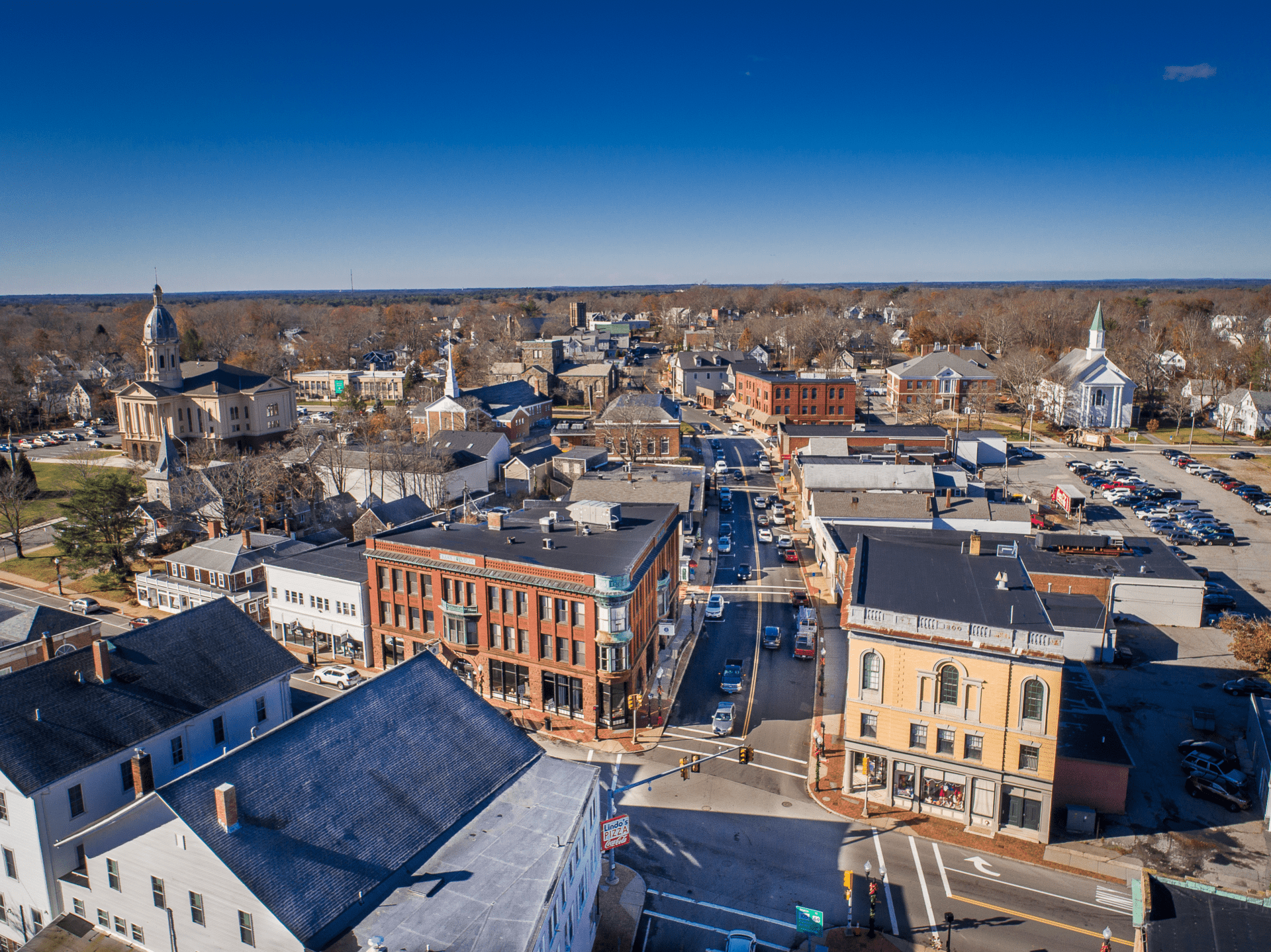 Aerial view of downtown North Attleborough showing historic brick buildings, streets, and church steeples under a clear blue sky.