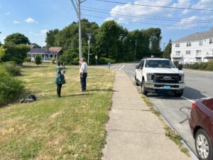 Two people talking on grass next to a road with a white truck
